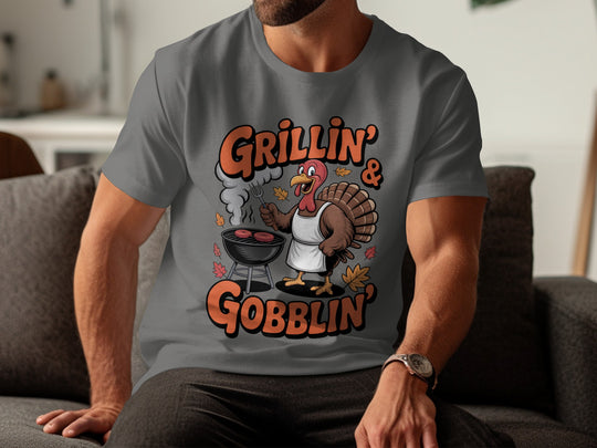 Person wearing a charcoal t-shirt with a turkey graphic and text 'Grillin' & Goblin' on a couch.