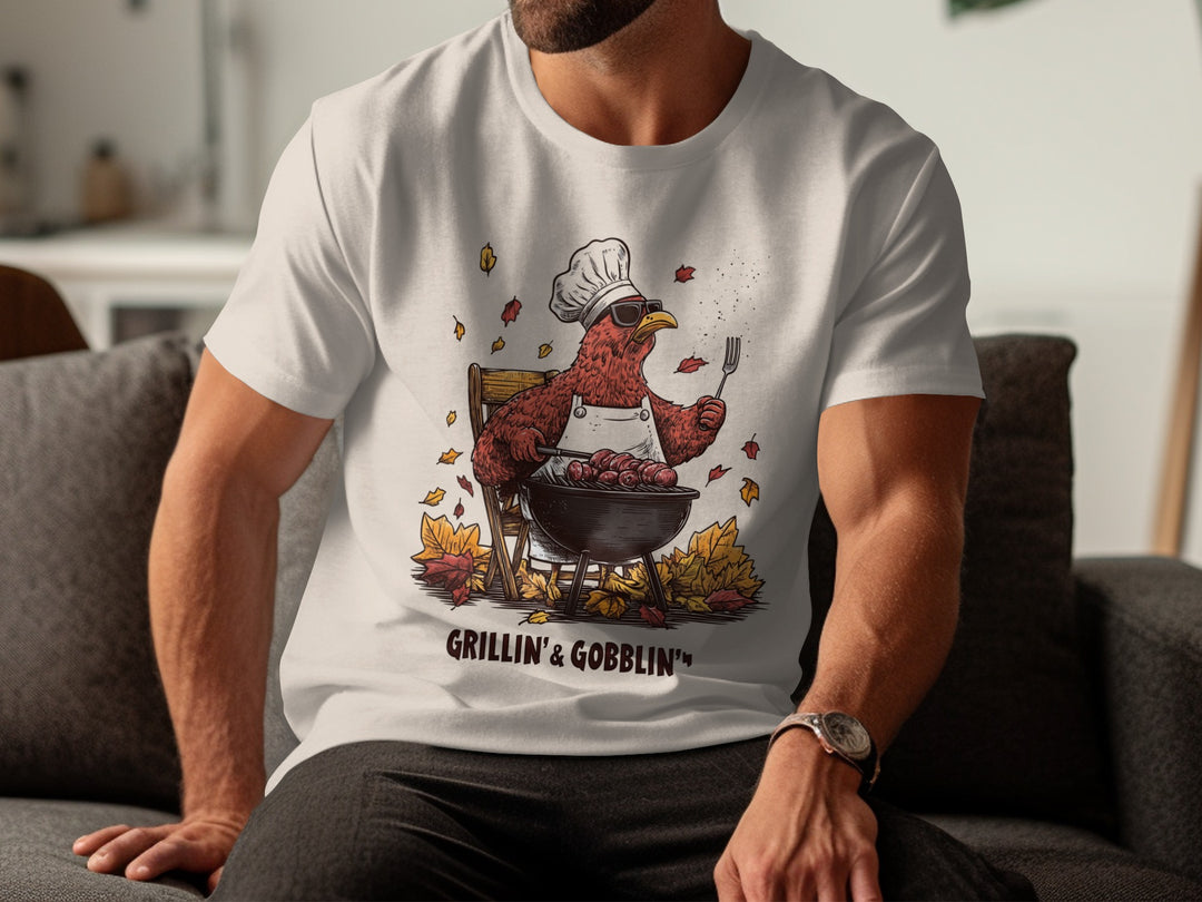 Person wearing a natural color t-shirt with a graphic design of a rooster in a chef hat and apron, sitting on a couch.