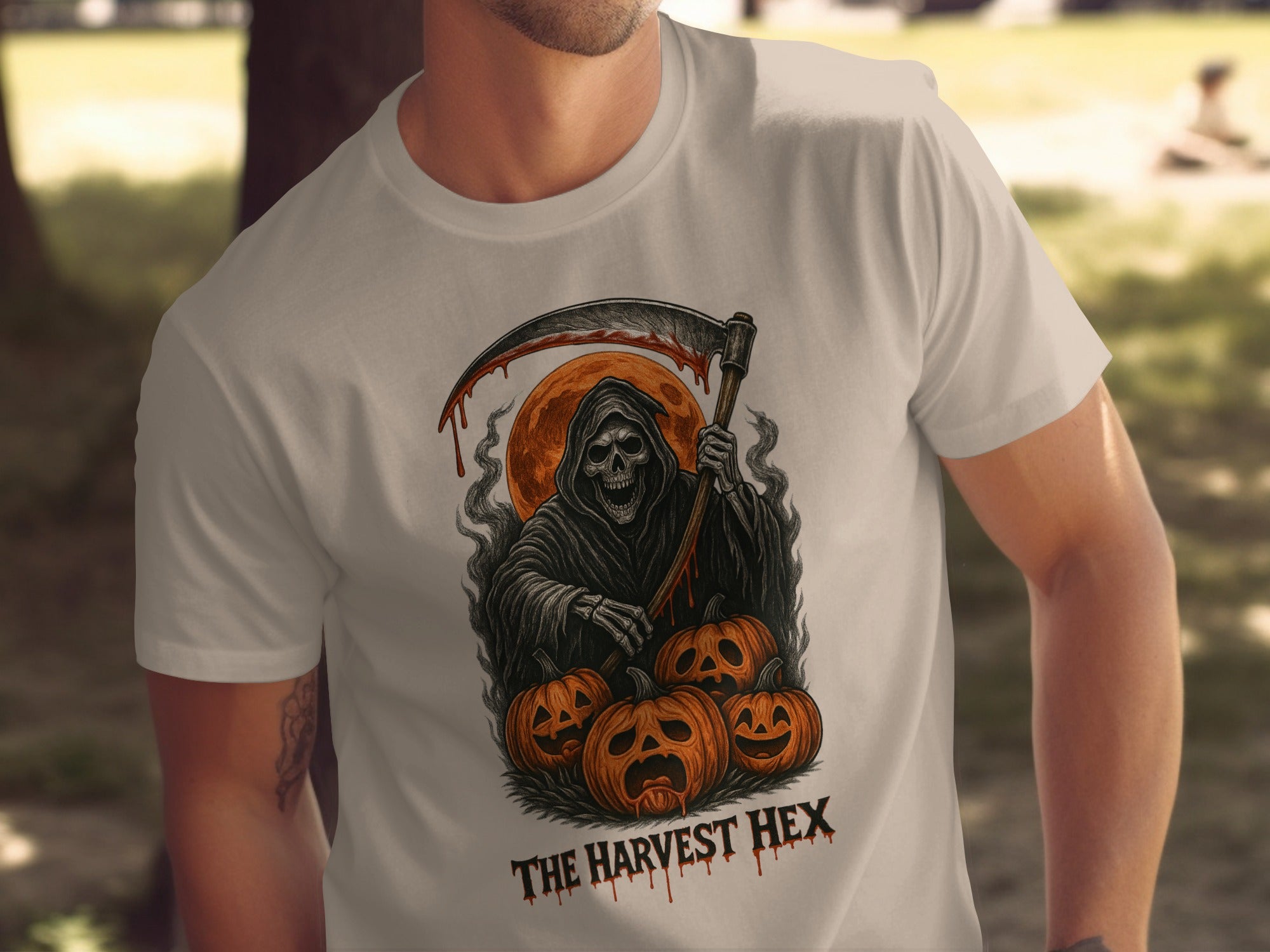 Person wearing a sand color t-shirt with a graphic design of a Grim Reaper and pumpkins, labeled 'The Harvest Hex'.