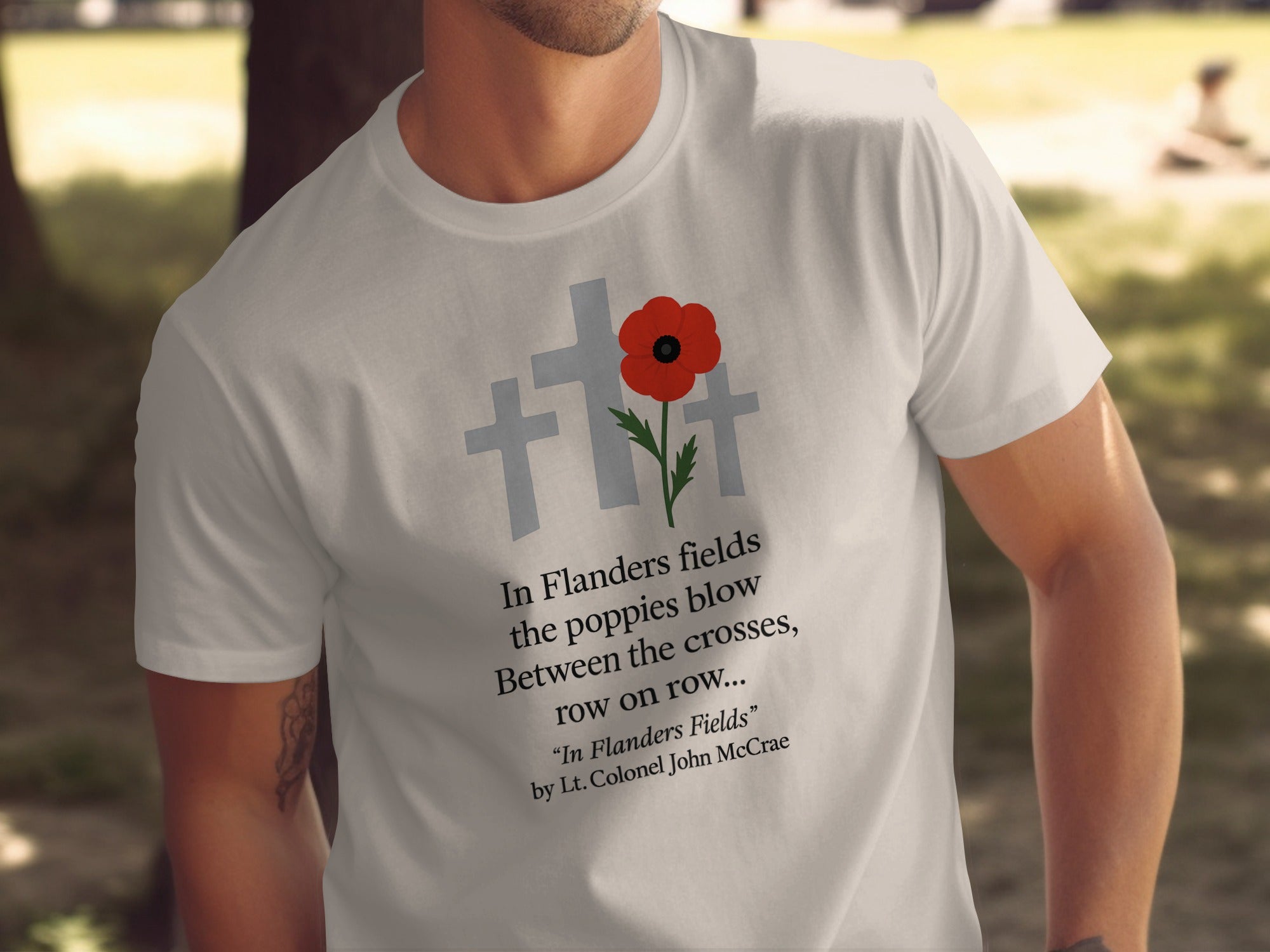 Person wearing a natural color t-shirt with a poppy design and text in a park setting