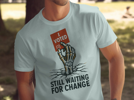 Person wearing a light blue t-shirt with a graphic of a hand holding an 'I Voted' card and text 'Still Waiting for Change'.