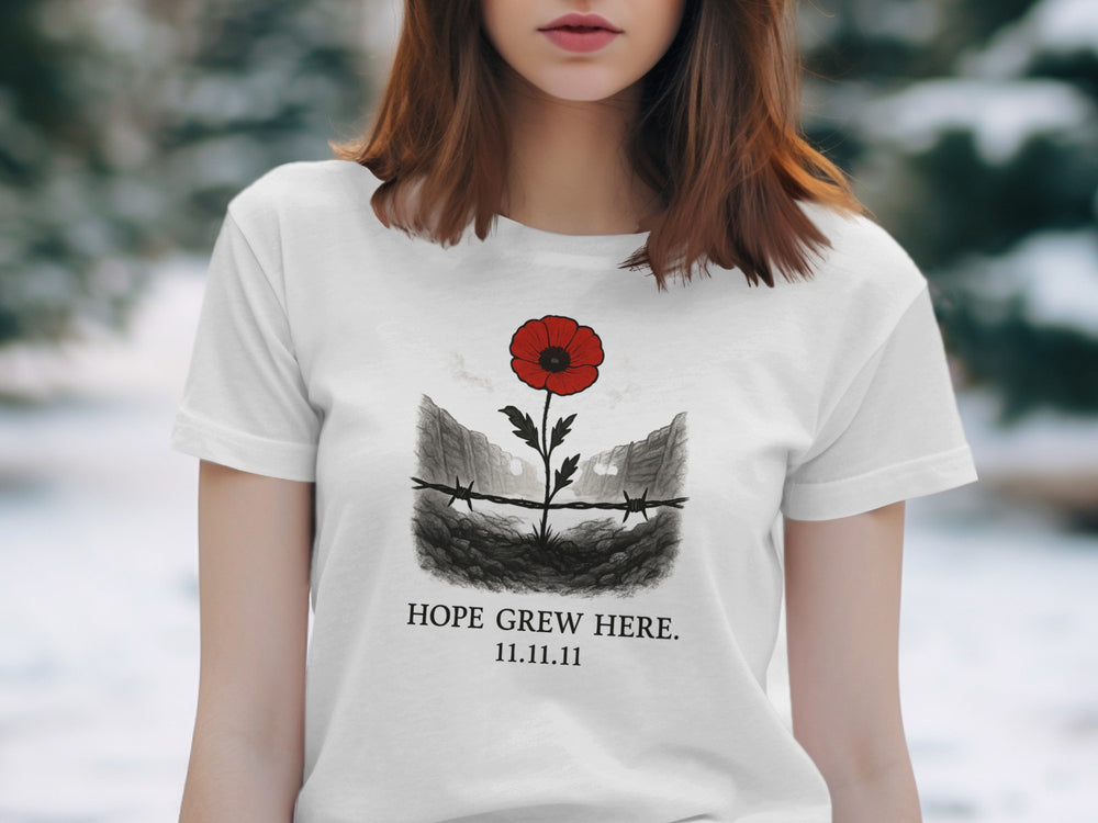 Person wearing a off white t-shirt with a red flower and barbed wire design, text 'HOPE GREW HERE. 11.11.11', outdoors.