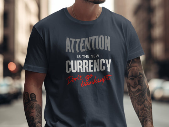 Person wearing a navy blue t-shirt with text 'Attention is the new currency. Don't go bankrupt.' on a city street.
