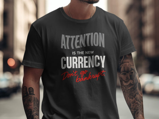 Person wearing a black t-shirt with text 'Attention is the new currency. Don't go bankrupt' on a blurred city street background.