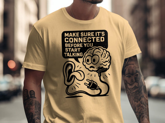 Person wearing a beige t-shirt with a graphic design and text in an urban setting