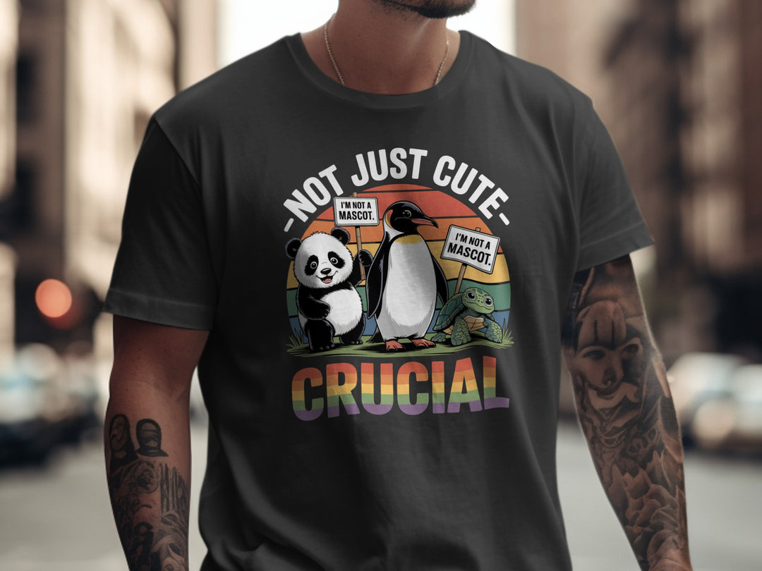 Person wearing a black t-shirt with a graphic of a panda, penguin, and crocodile with text 'Not Just Cute, I'm Also Crucial' on a blurred city street background.