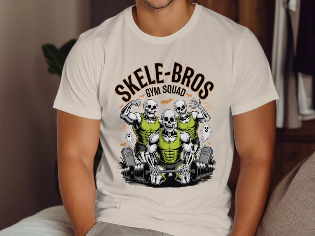 Person wearing a natural color t-shirt with 'SKELE-BROS GYM SQUAD' design featuring skeletons lifting weights.