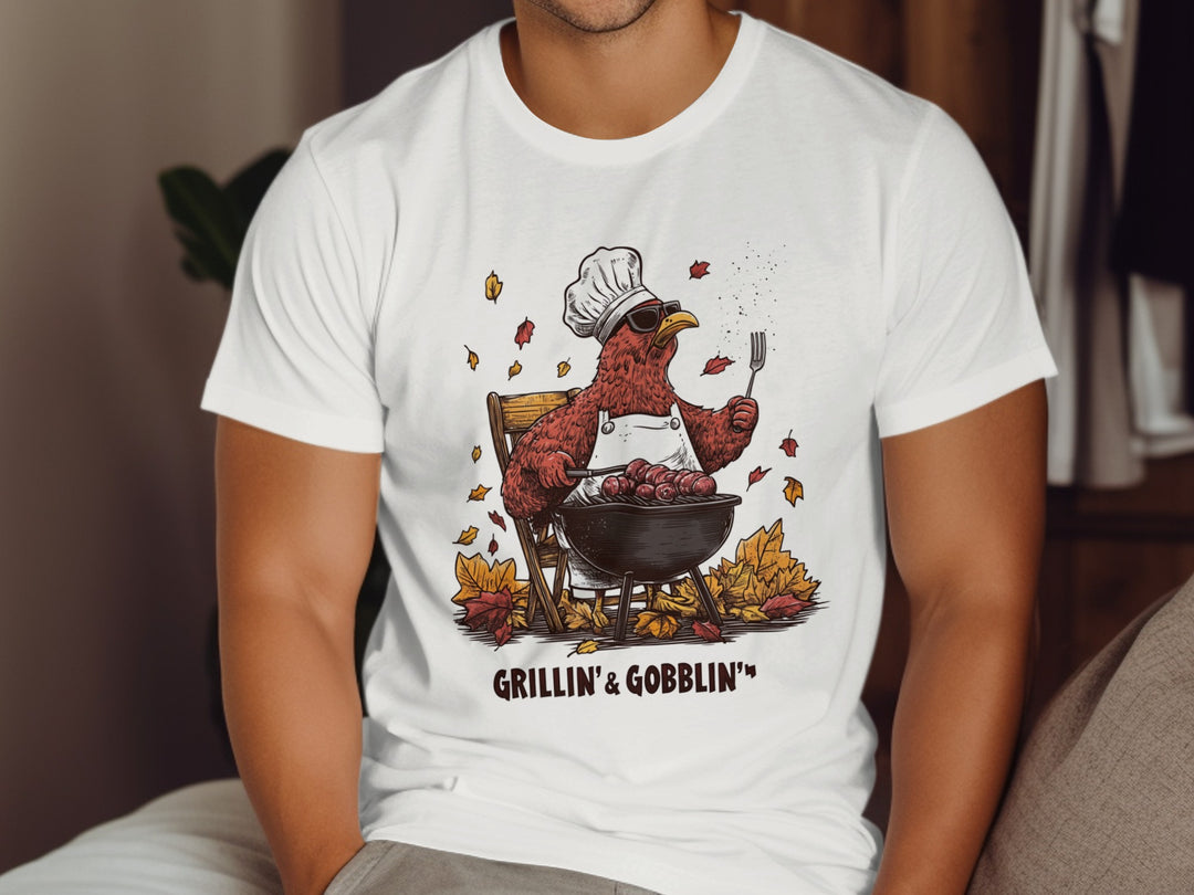 Person wearing a white t-shirt with a graphic of a turkey grilling and text 'GRILLIN' & GOBBLIN'.