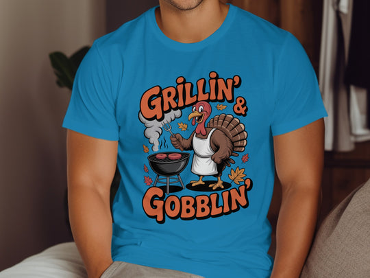 Person wearing a blue t-shirt with a graphic design of a turkey and text 'Grillin' & Gobblin'.