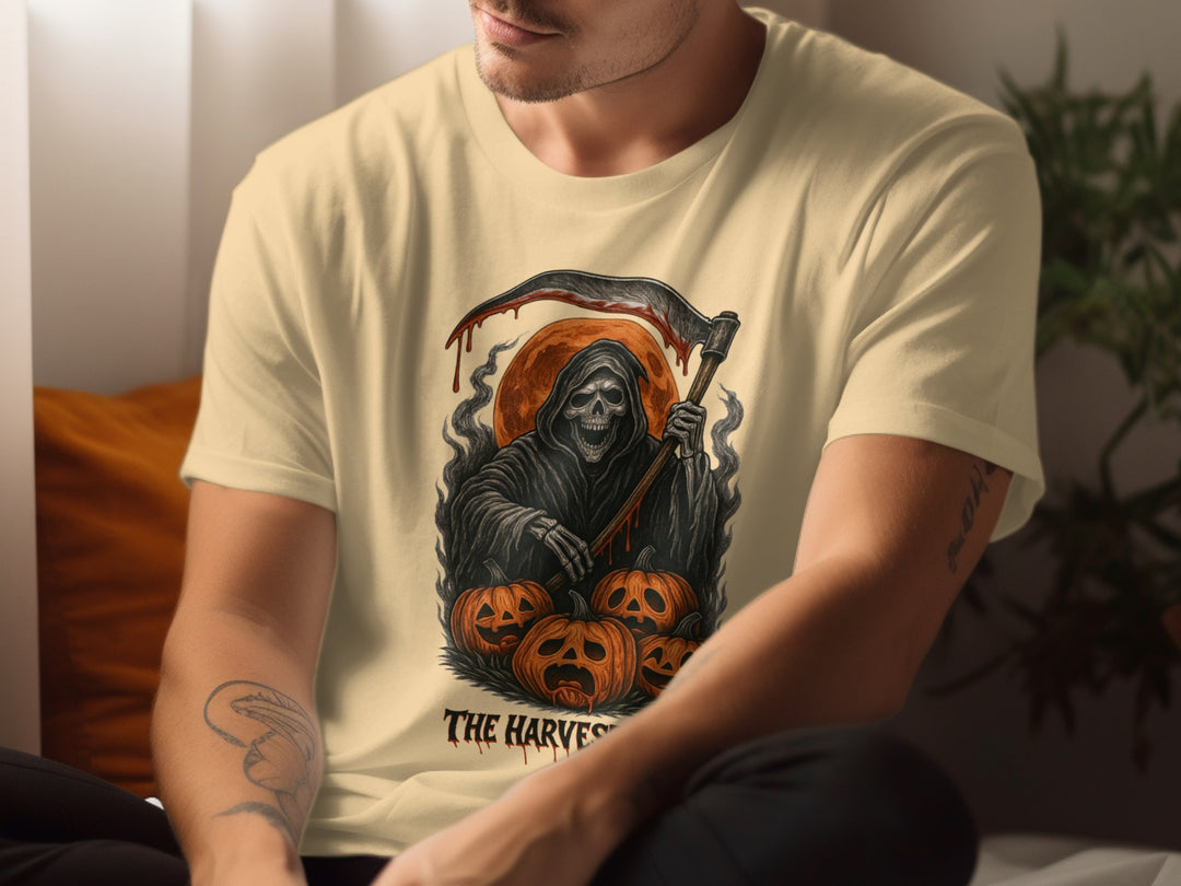 Person wearing a beige t-shirt with a graphic design of a skeleton holding an axe and pumpkins, with text 'The Harvest'.
