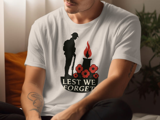 Person wearing a natural color t-shirt with a 'Lest We Forget' design featuring a soldier, candle, and poppies.