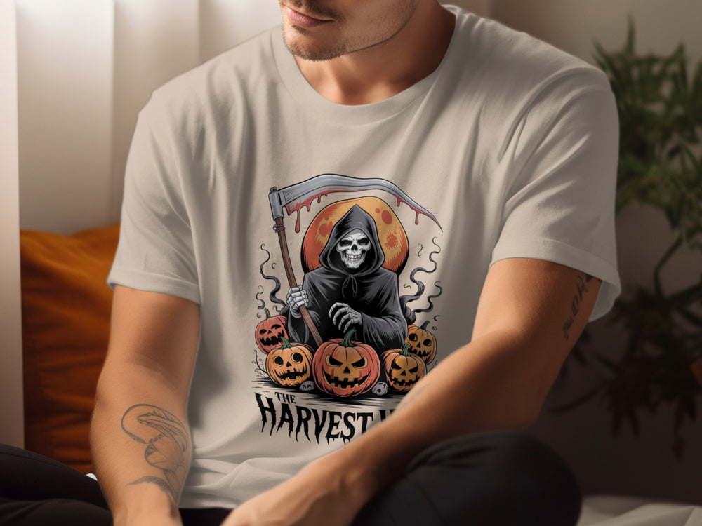 Person wearing a sand color t-shirt with a graphic design of a skeleton holding an axe and pumpkins.