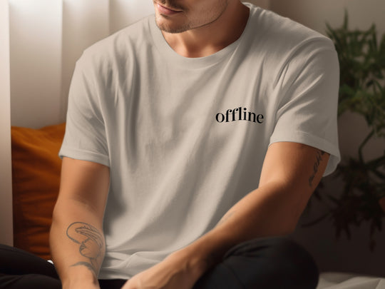 Person wearing a sand color t-shirt with 'offline' text, sitting indoors.