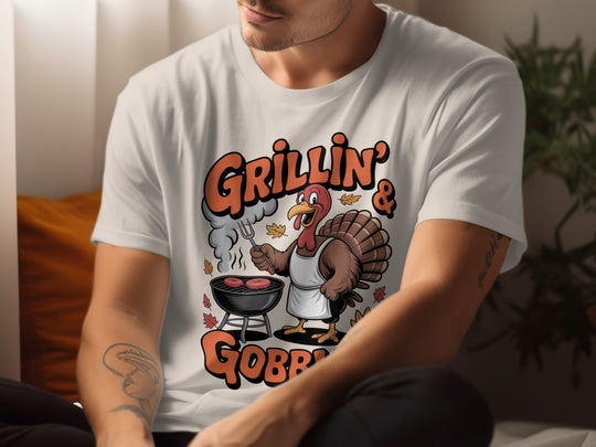 Person wearing a natural color t-shirt with a turkey graphic and text 'Grillin' & Gobbling'.