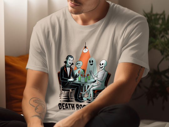 Person wearing a sand color t-shirt with a graphic design of skeletons at a table with a bottle labeled 'Death Row'.