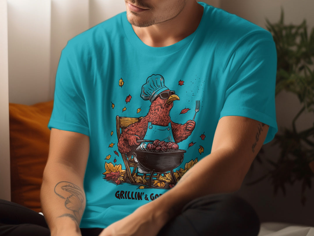 Person wearing a turquoise t-shirt with a graphic of a rooster cooking on a grill.