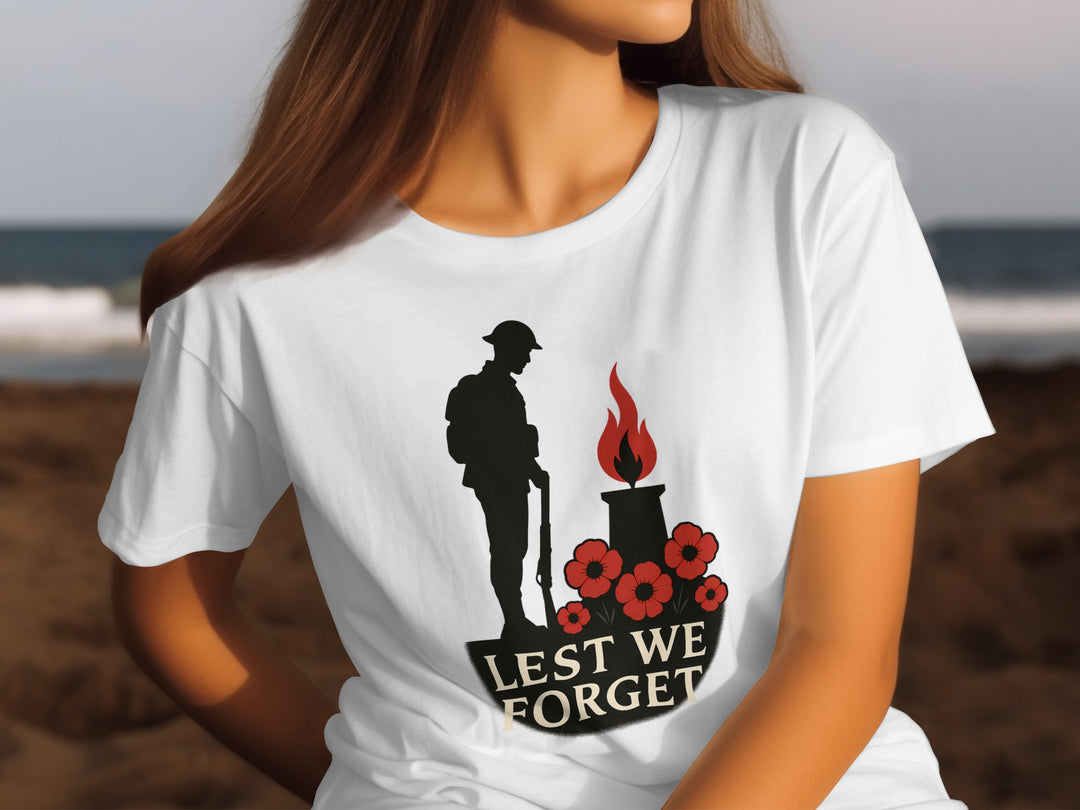 Person wearing a white t-shirt with a memorial design featuring a silhouette of a soldier, a flame, and poppies with 'Lest We Forget' text.