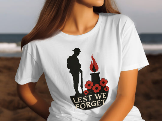 Person wearing a white t-shirt with a memorial design featuring a silhouette of a soldier, a flame, and poppies with 'Lest We Forget' text.