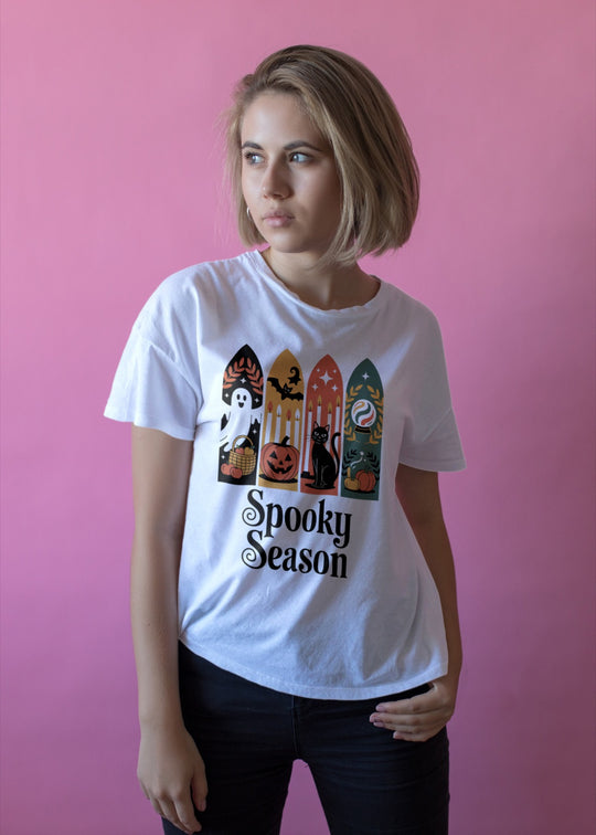 Women wearing a white t-shirt with Halloween-themed design against a pink background