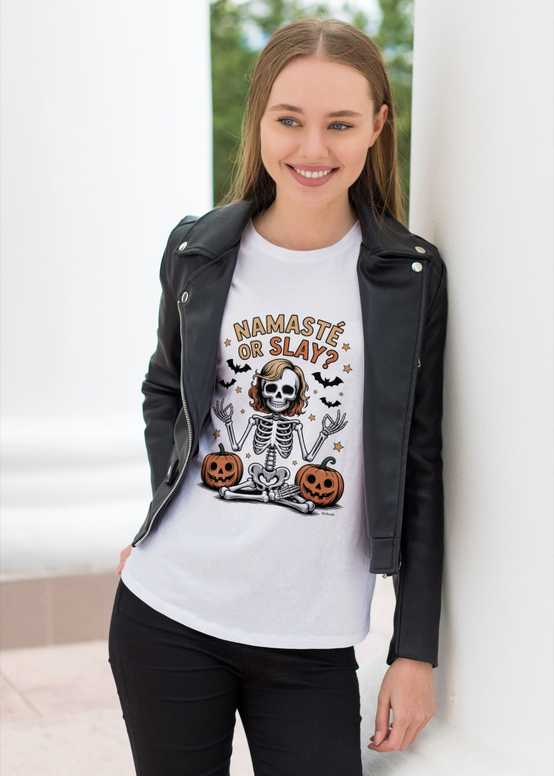 Woman wearing an off white t-shirt with a skeleton design and text, standing against a white wall.