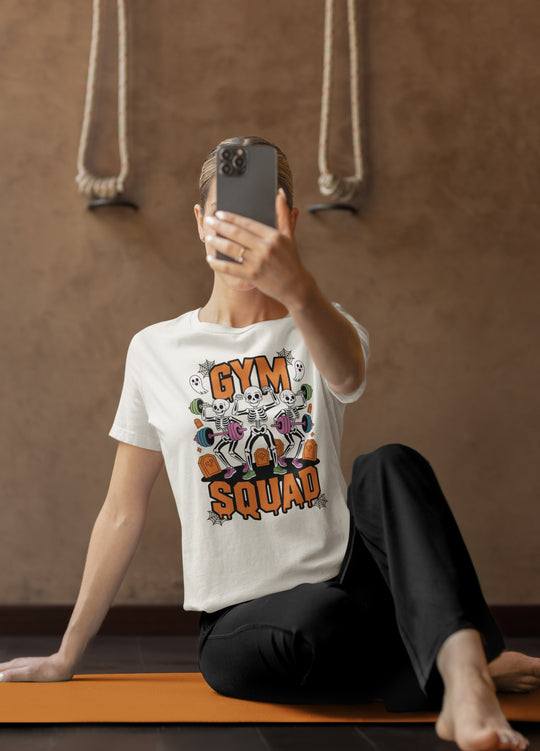 Women wearing a 'Gym Squad' t-shirt taking a mirror selfie on a yoga mat.