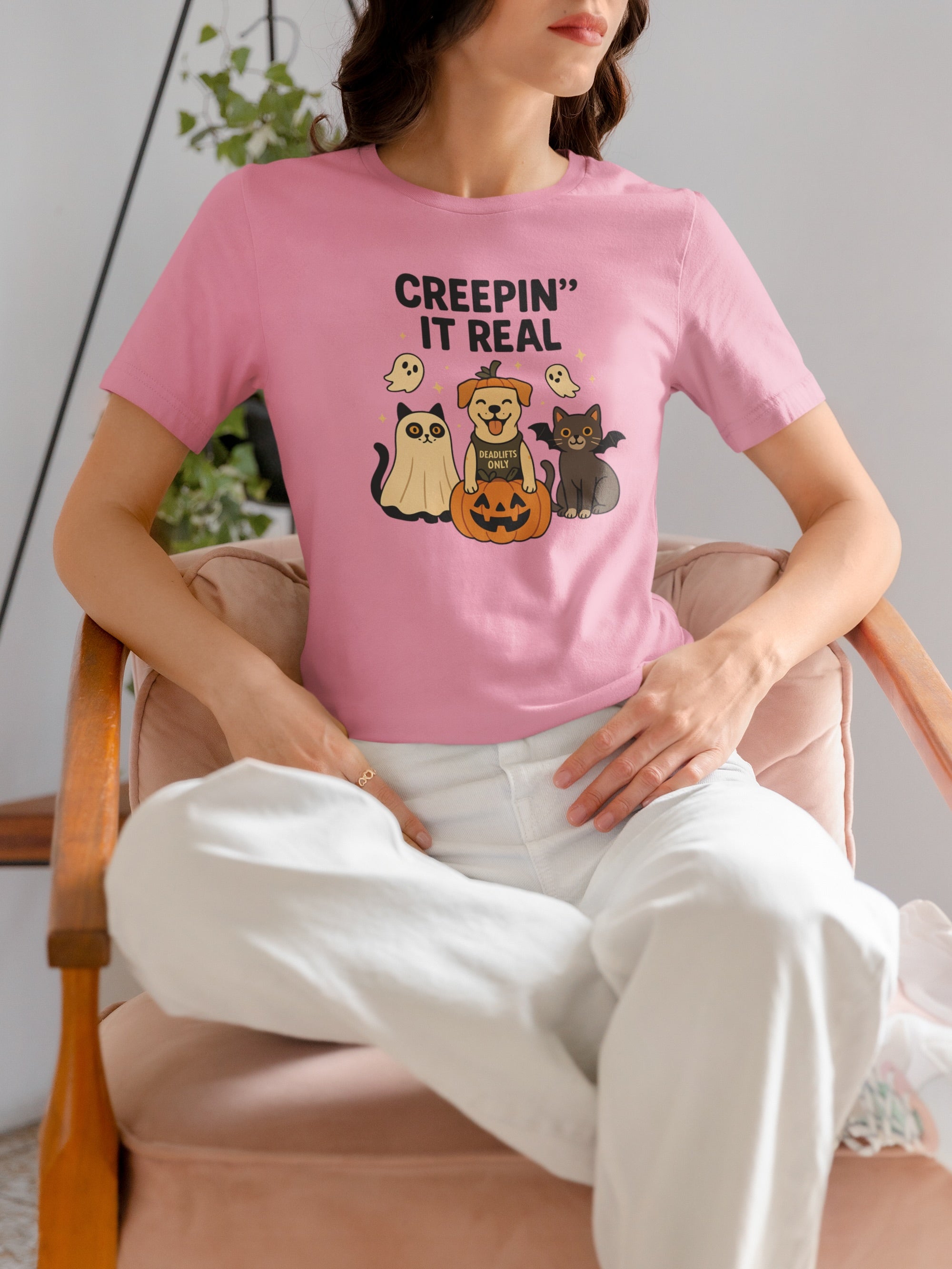 Women wearing a pink t-shirt with Halloween-themed graphics sitting on a chair.