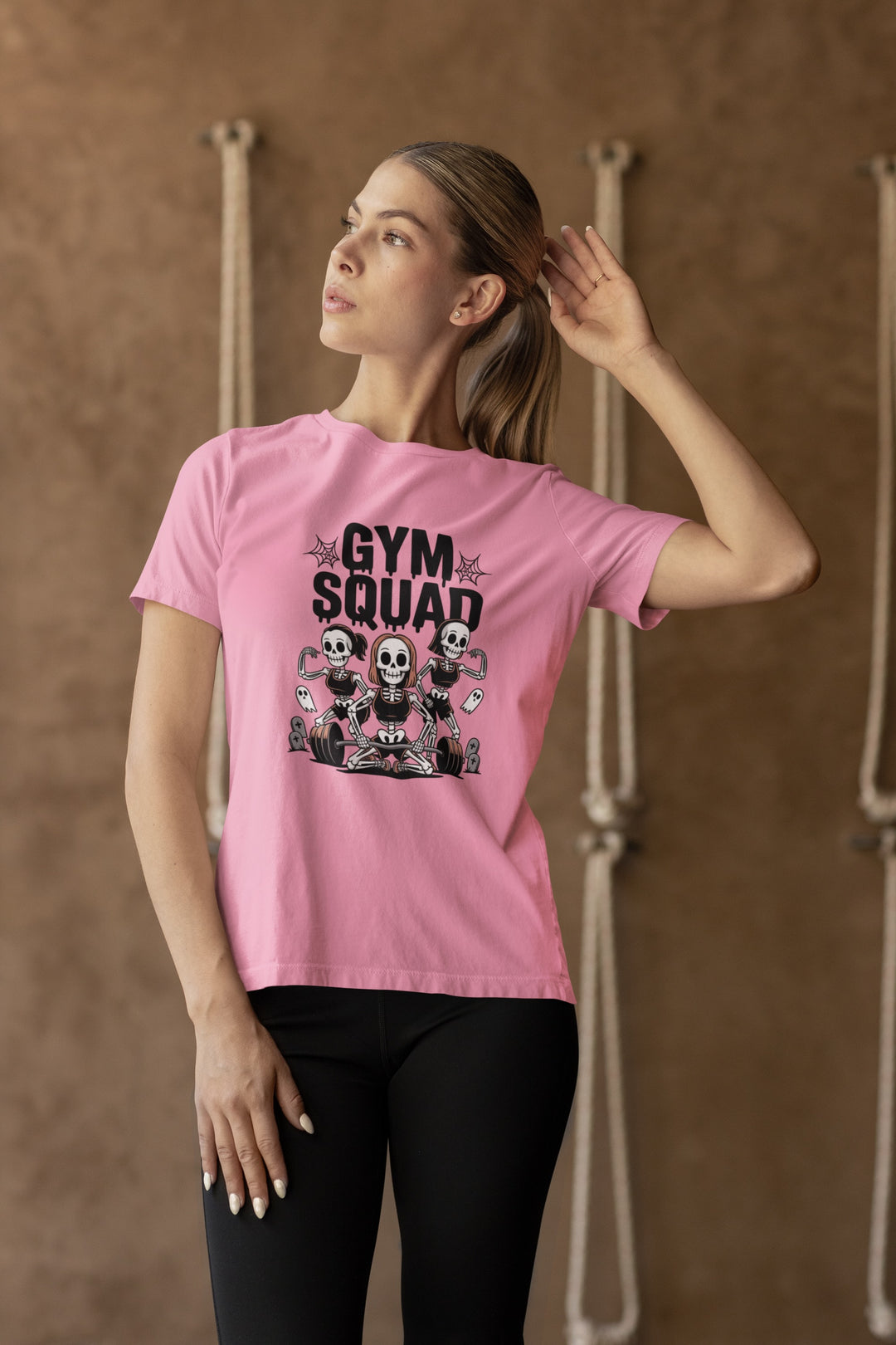 Woman wearing a pink t-shirt with 'Gym Squad' graphic design against a brown background