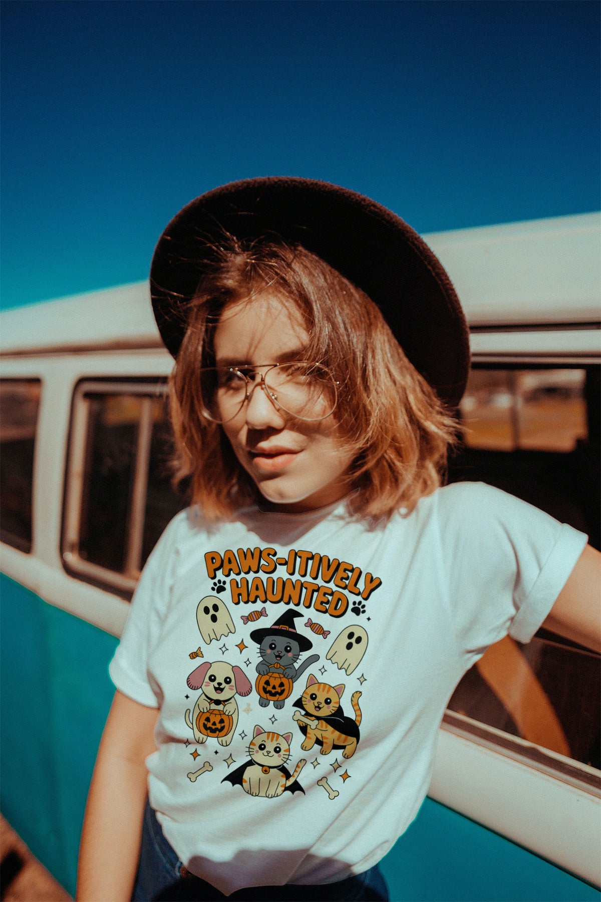 Women wearing a 'Paws-itively Haunted' t-shirt in front of a vintage van.